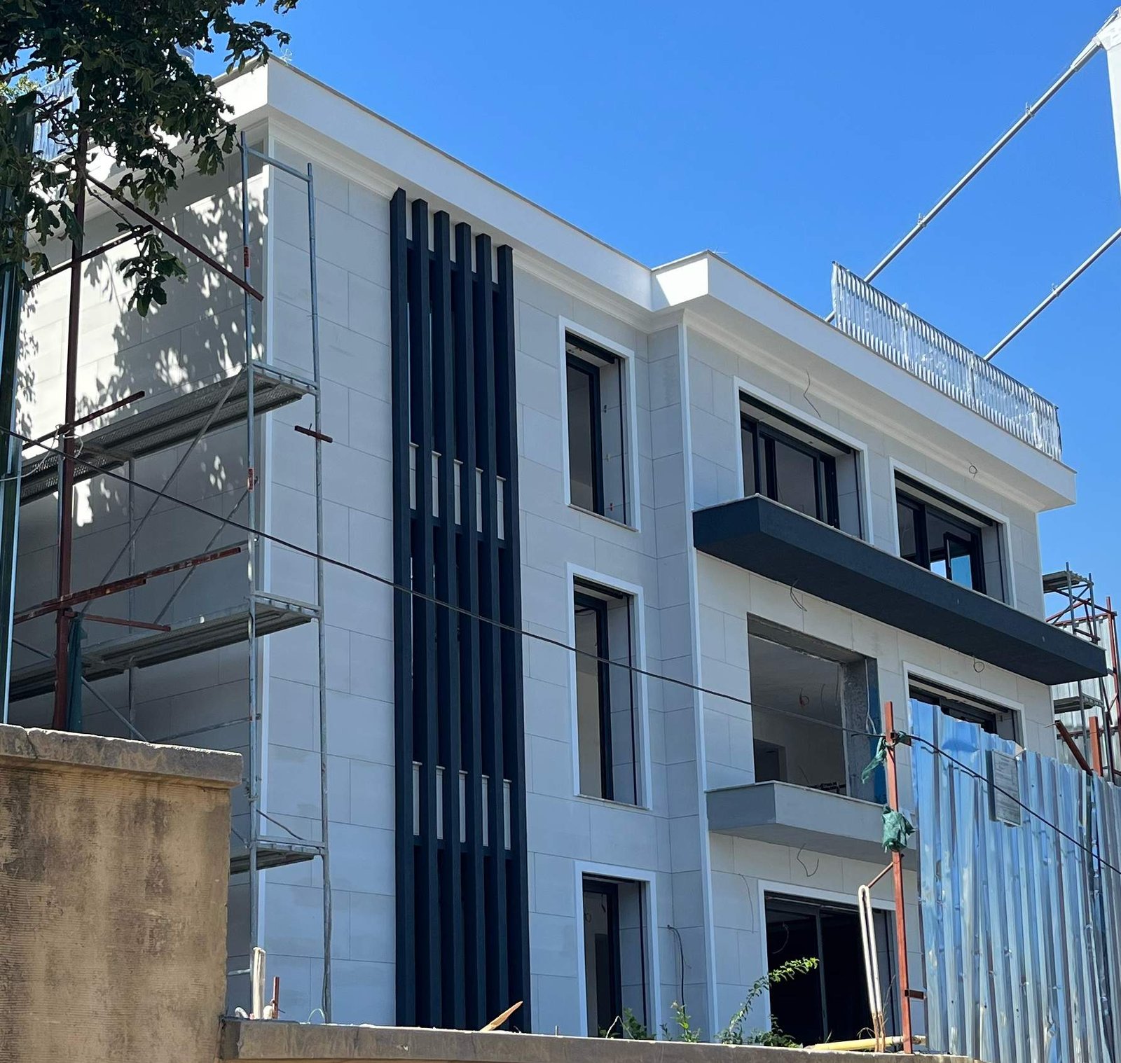 Özel villa dış cephesinde açık renk yüzeyler, koyu düşey elemanlar ve balkonlar.